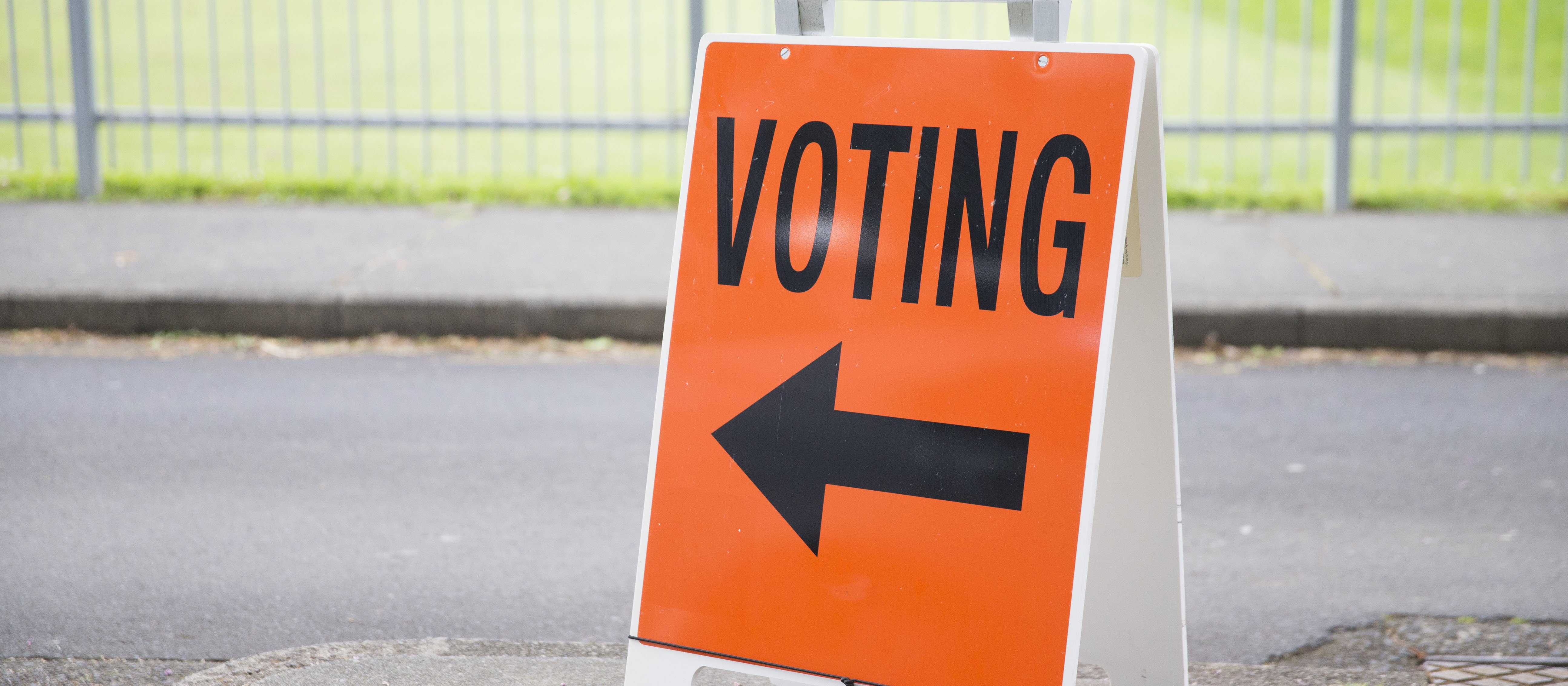An orange voting sign on a street, with an arrow pointing the way