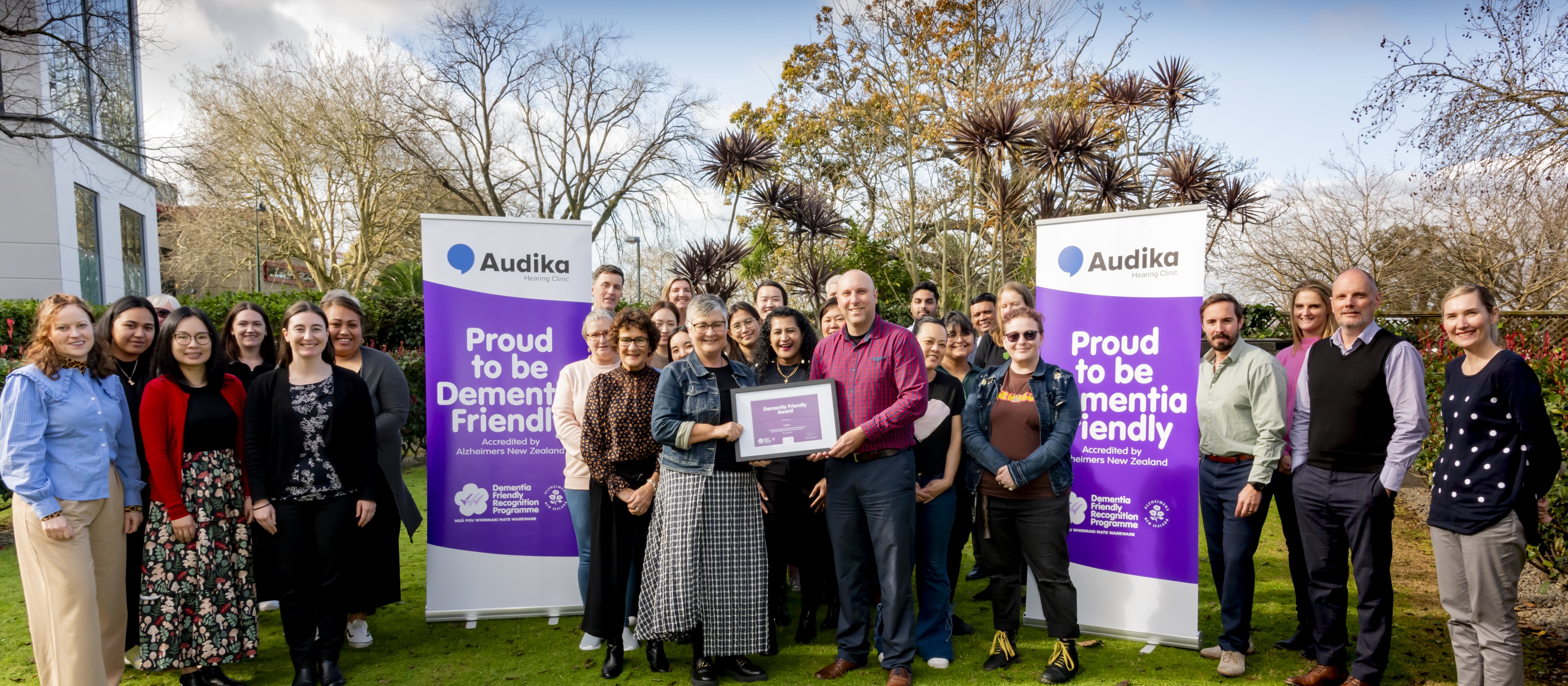 A group of people standing on lush grass, two in the middle holding up a framed certificate