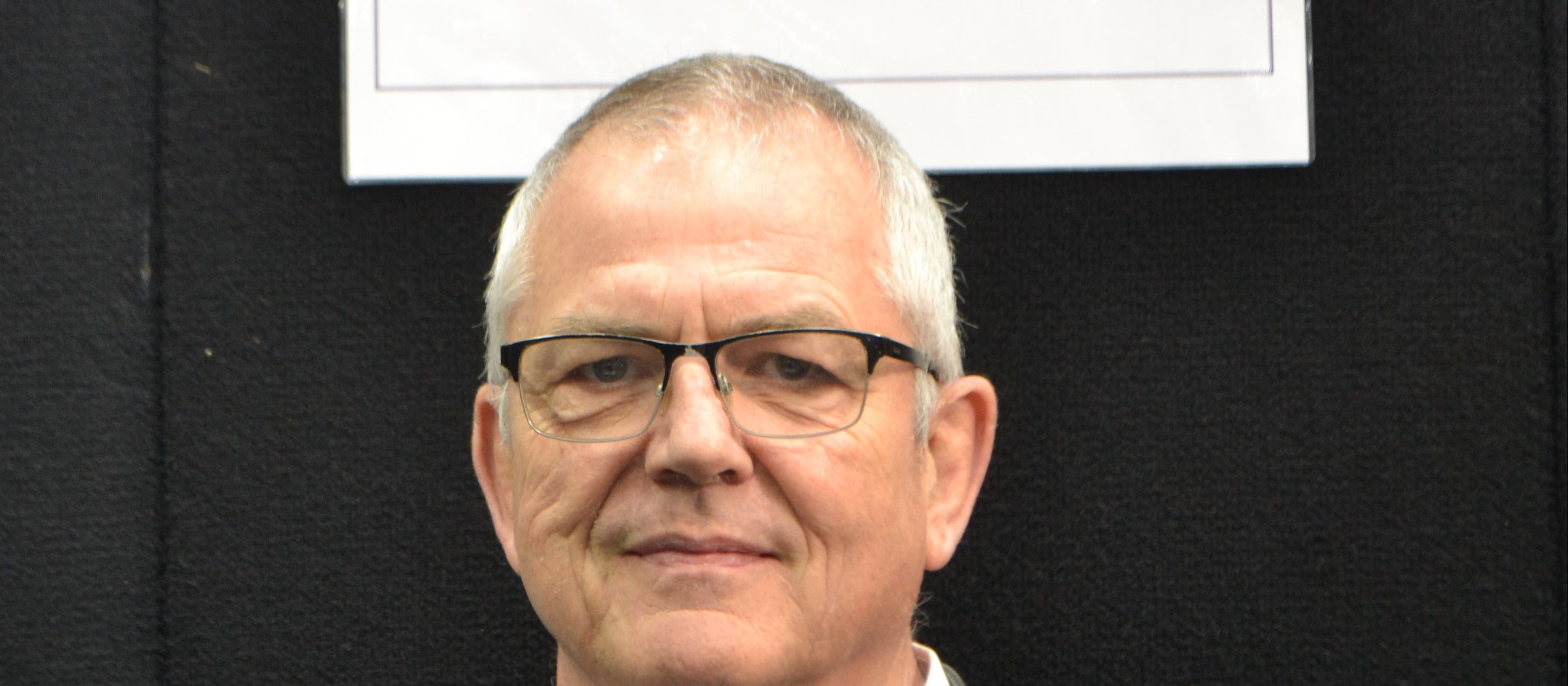 Man with glasses looking at camera, sign above head reads Compound Labs