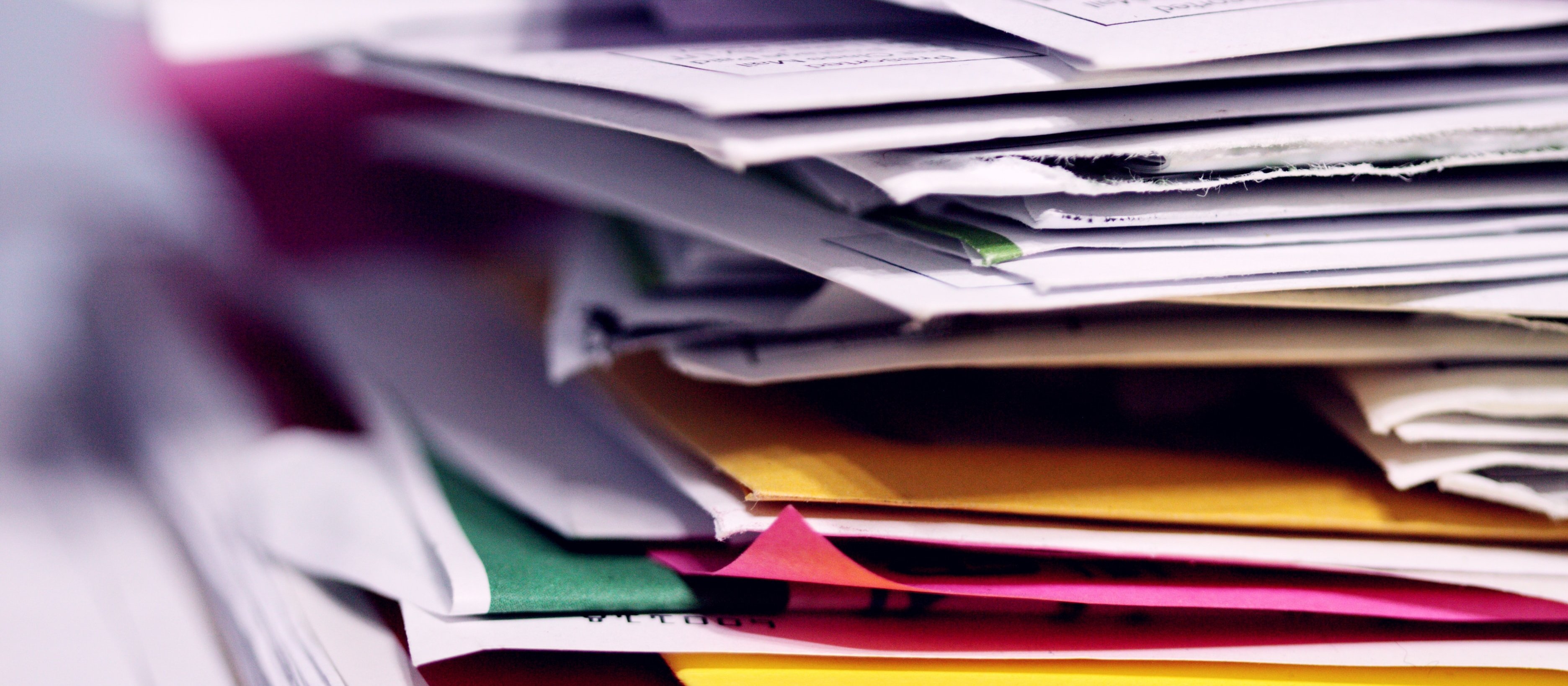 Image shoes a stack of documents and reports, some in colourful folders