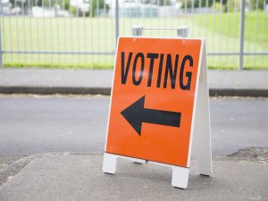 An orange voting sign on a street, with an arrow pointing the way