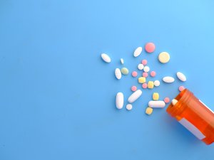 Different coloured pills spilling out of a medication jar on a blue background